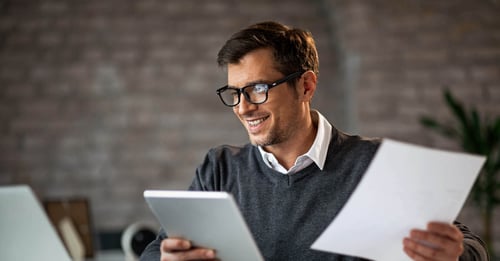 Chiffres cles mandataires immobiliers - Homme souriant au bureau en tenant un bloc notes