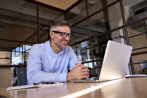 Homme assis au bureau et souriant en regardant son ordinateur