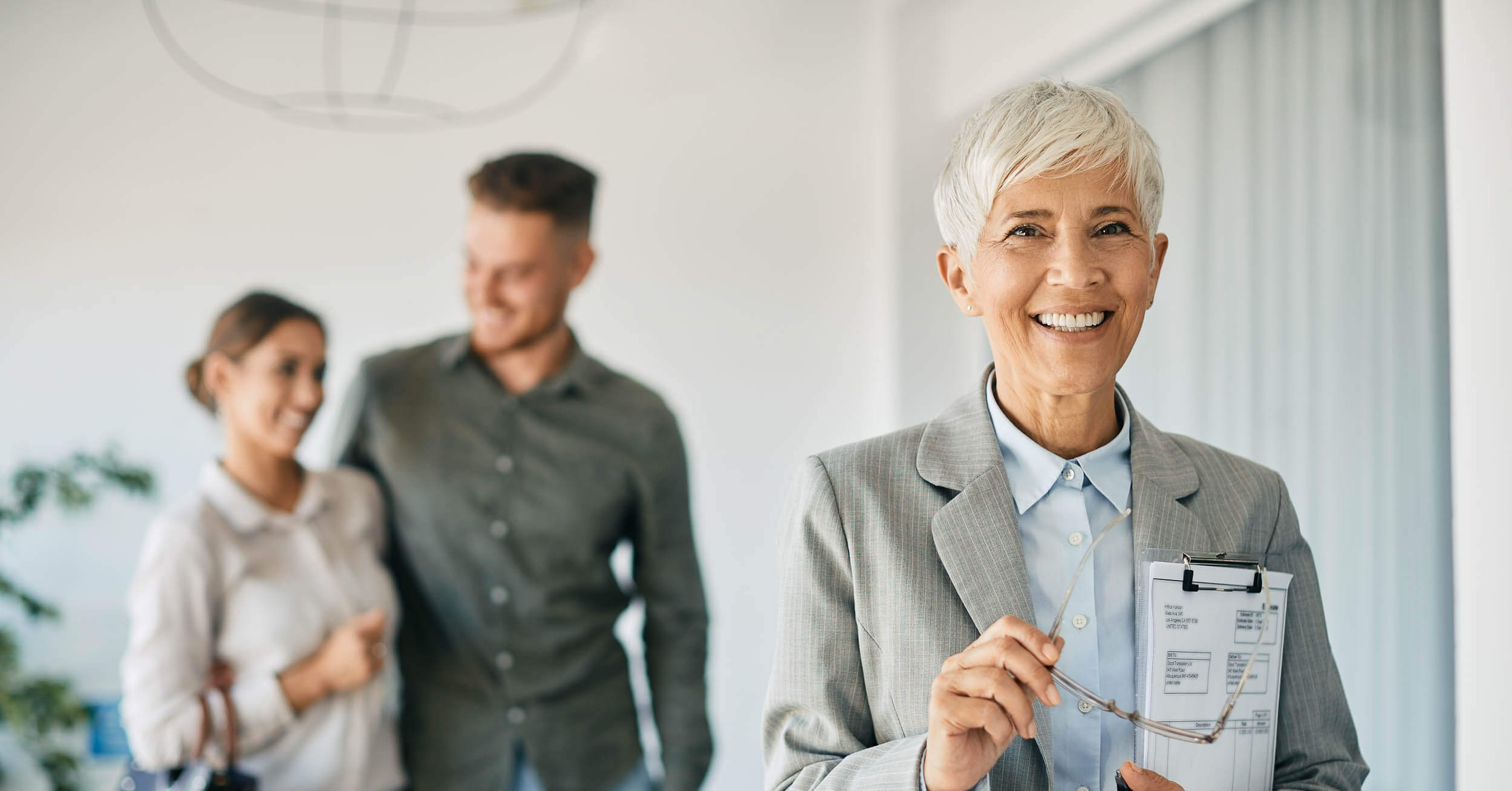 Devenir mandataire immobilier independant - Femme mandataire immobilier qui sourit avec un couple heureux en arriere plan