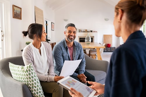 Couple assis sur un canapé en discussion avec un mandataire immobilier